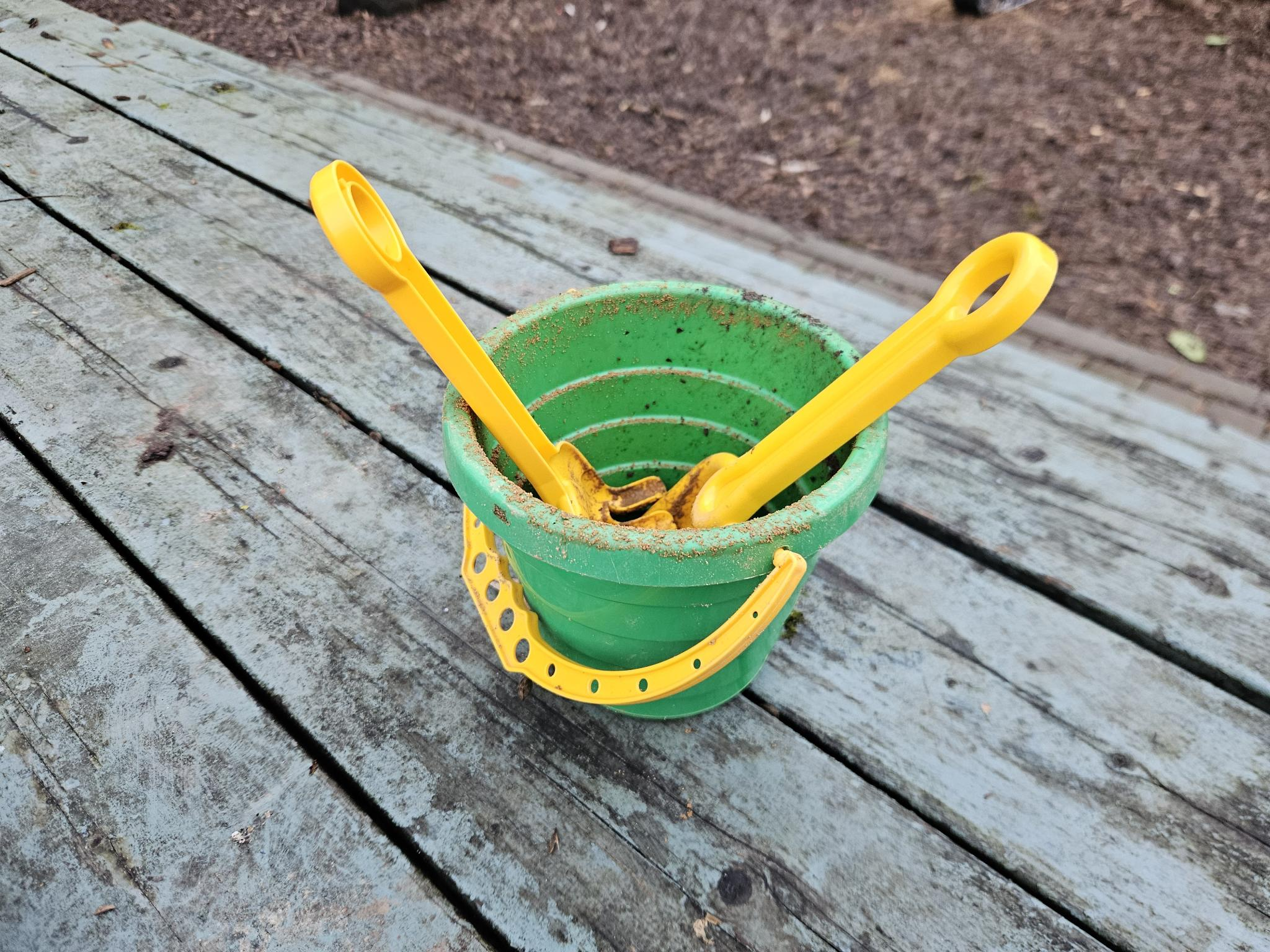 Ein grüner Spielzeugeimer mit Harke und Schaufel